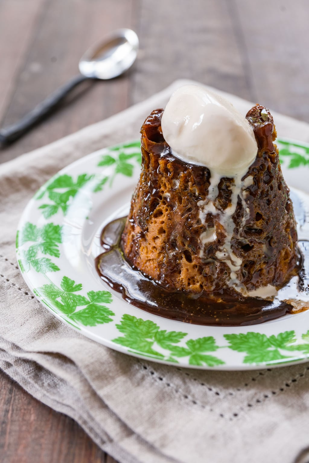 Molten, gooey Sticky Toffee Pudding with rich caramel sauce pouring down  the sides and vanilla ice cream melting on top.