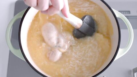 Stirring Arroz Caldo with a spatula.