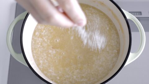 Sprinkling salt into Arroz Caldo to adjust to taste.