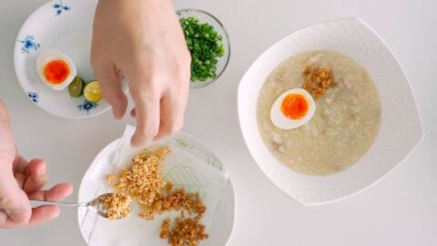 Condiments for Arroz Caldo including soft boiled egg, scallions, crisp garlic, chicken chicharron, and Calamansi.