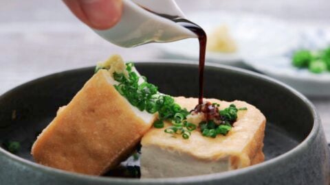 Pouring soy sauce onto Atsuage with scallions and ginger.