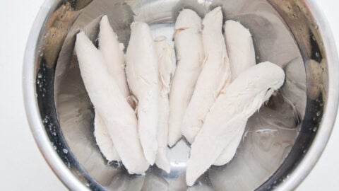 Poached chicken tenders for bang bang chicken chilling in a bowl of ice water.