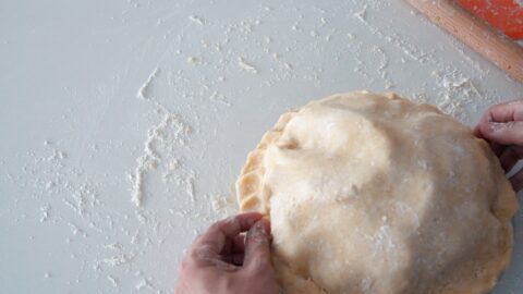 Fluting the edges of the apple pie with fingers.