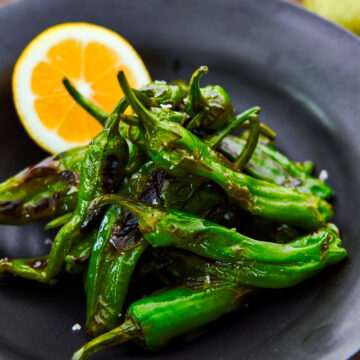 Char-grilled blistered shishito peppers with smoked salt and lemon.