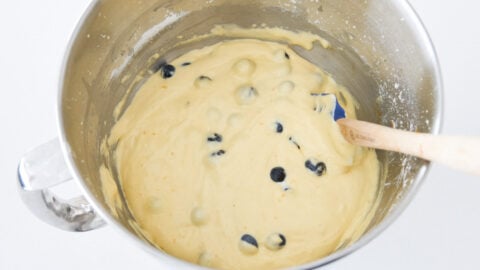 Blueberries in olive oil cake batter in a stainless steel bowl.