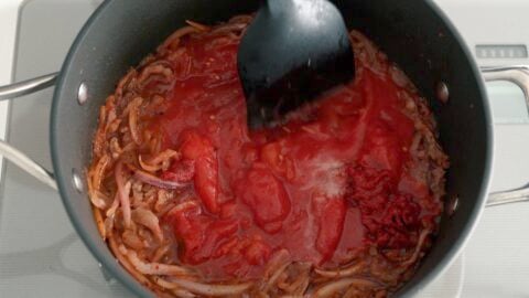 Chopping up stewed tomatoes in Amatriciana sauce using a spatula.