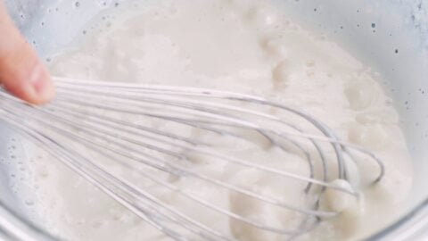 Whisking partially cooked mochi in a glass bowl.