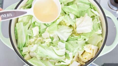 White wine being added to a green dutch oven full of cabbage for making chicken stew.