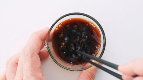 Whisking sushi bowl sauce in a glass bowl with chopsticks.