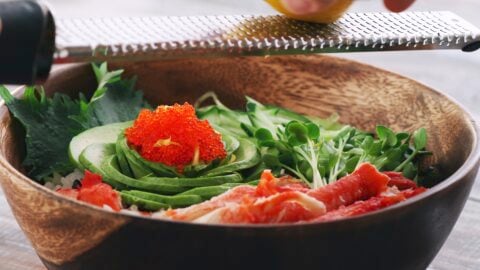 Grating yuzu zest onto a California Roll sushi bowl.