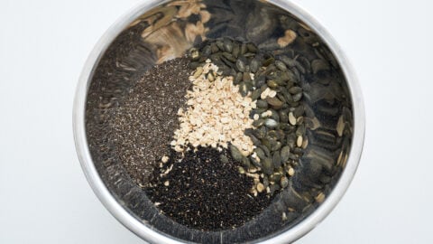 Rolled oats, pumpkin seeds, black sesame seeds, and chia seeds in a stainless steel bowl for making savory granola bars.