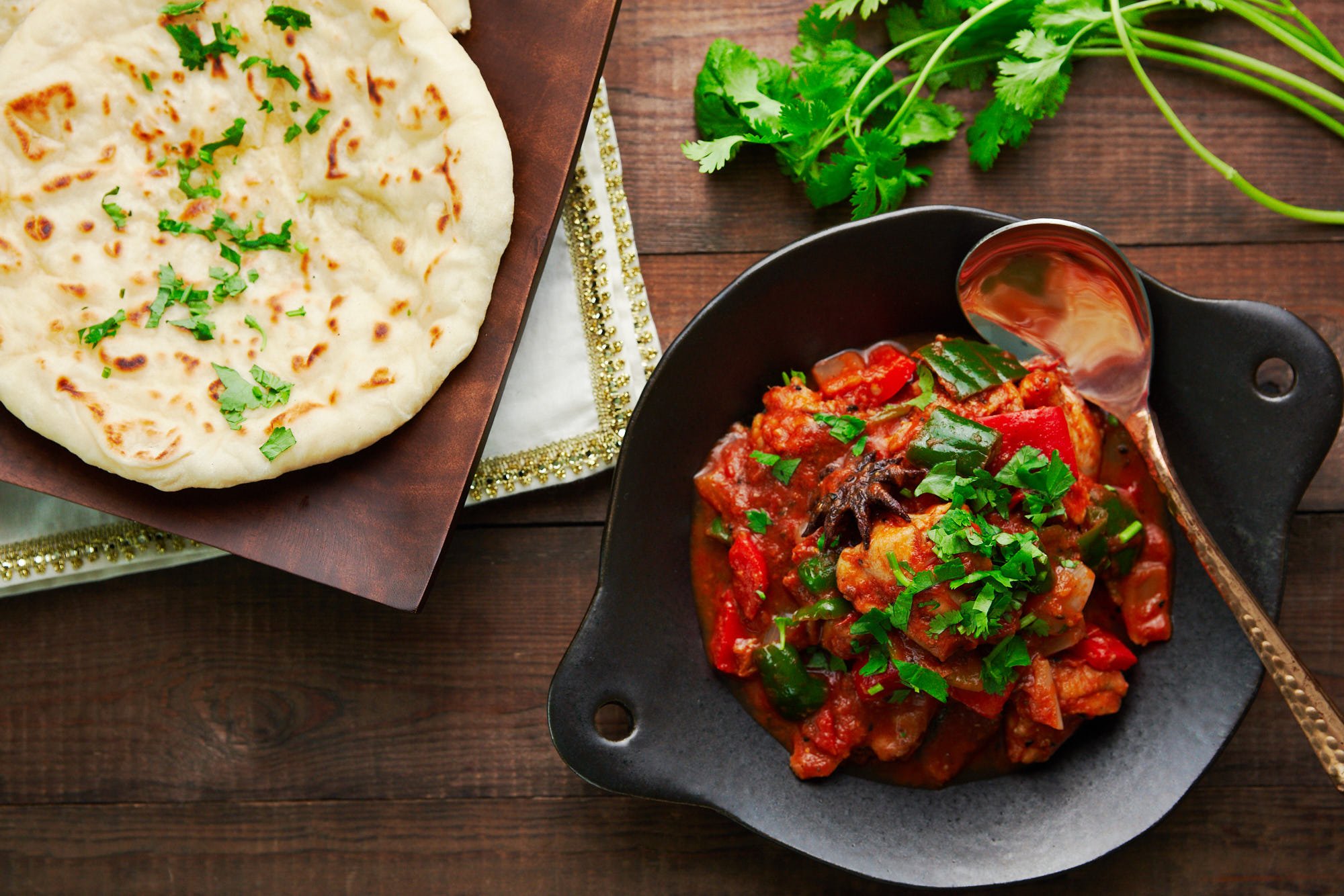 Buttered naan on a wooden plate with a serving of Chicken Jalfrezi with peppers, onions, and tomatoes.