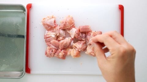 Sprinkling salt and pepper onto chicken thighs.