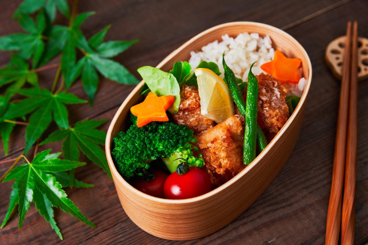 Karaage (Japanese fried chicken) in a wooden bento box with rice, lemon, carrots, tomatoes, and broccoli. Karaage is one of the most popular bento items in Japan.