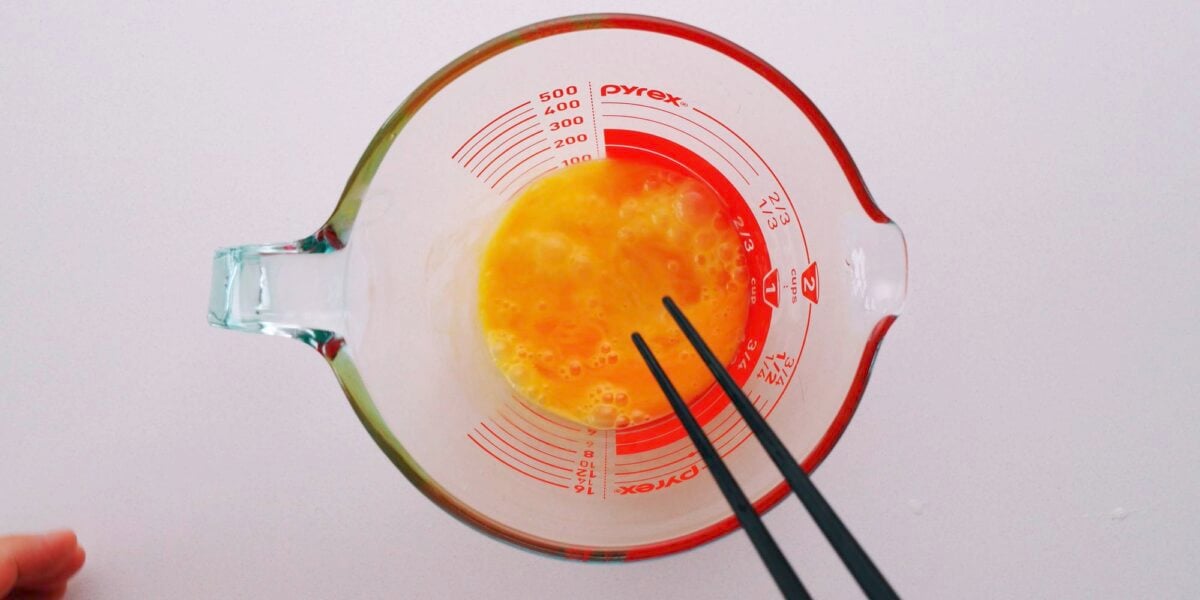 Lightly beating eggs for katsudon in a glass cup with chopsticks.