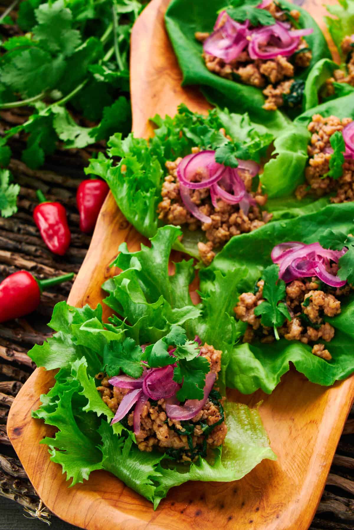 A delectable platter of Asian Chicken Lettuce Wraps garnished with fresh cilantro and pickled red onions.