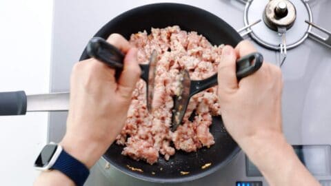 Chopping up ground chicken with two spatulas.