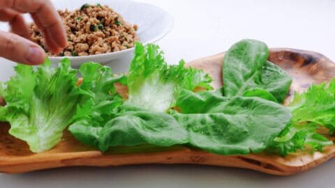 Lettuce leaves lined up on a wooden platter with basil chicken stir-fry in the background.