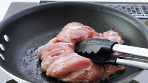 Pan-frying skin-side of chicken while pressing down on it with tongs.