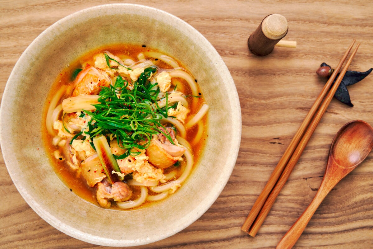 Chicken Udon noodle soup with chicken, egg, and scallions, garnished with shichimi togarashi.