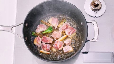 Chicken and scallions in a pan being deglazed with sake.