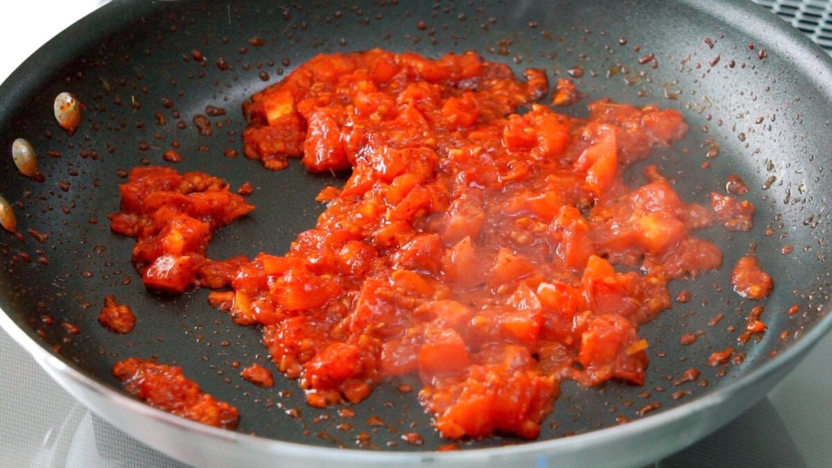 Fresh tomatoes being cooked down in a frying pan with garlic and chili flakes.