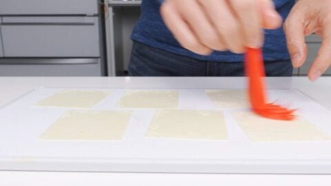 Brushing sesame oil onto wonton wrappers with a red pastry brush.