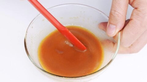 Whisking Chinese Chicken Salad dressing together in a glass bowl with a small spatula.