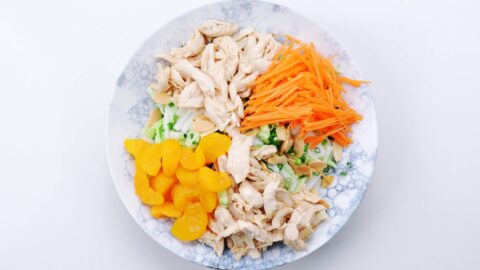 Mandarins and julienned carrots along with shredded chicken on an Asian chicken salad.