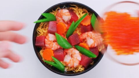 Chirashi sushi bowl topped with tuna, shrimp, eggs, carrots and snap peas.