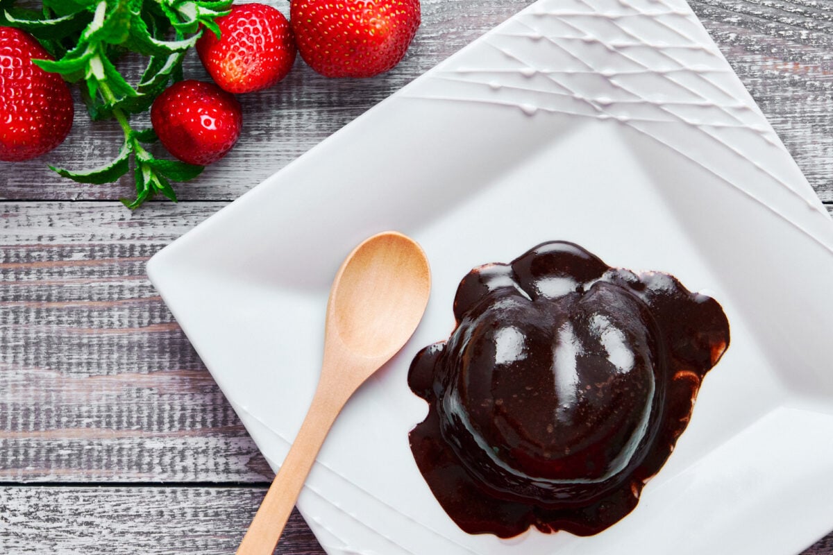 Rich decadent chocoalte mug cake served on a white plate with strawberries.