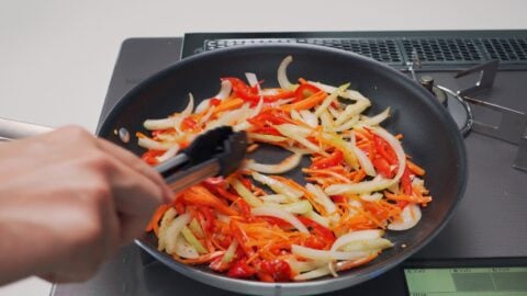 Stir-frying carrots, celery, onions and bell peppers in a frying pan.