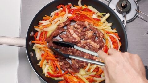 Browning marinated pork in a frying pan with vegetables for making Chop Suey.