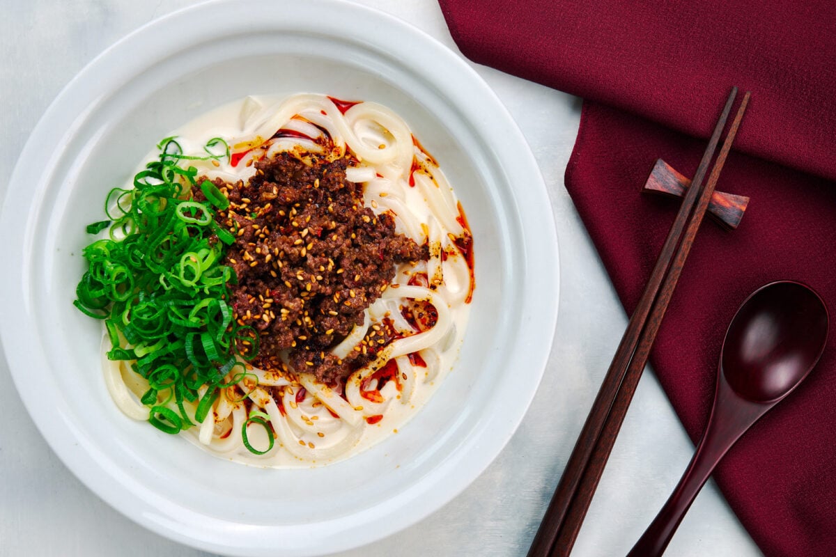 A bowl of Hiyashi Tantan Udon noodles in a rich sesame broth topped with spicy beef and chili oil.