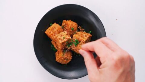 Garnishing crispy tofu bites with scallions.