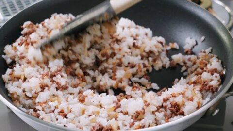 Rice, caramelized onions and ground beef in a pan for making curry fried rice.