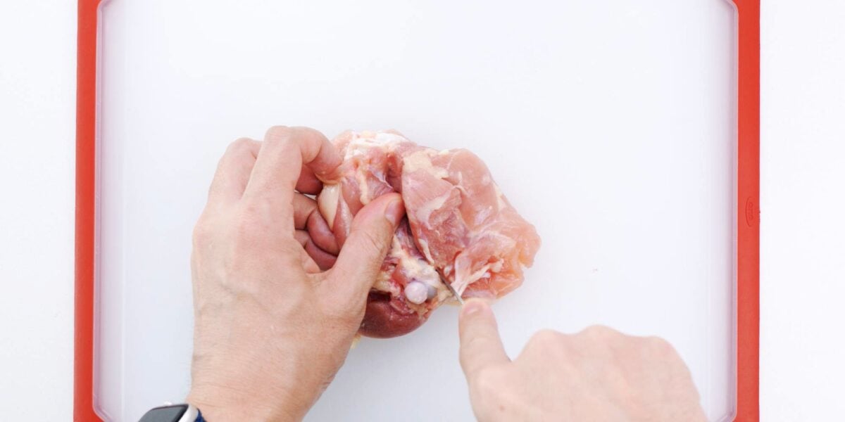 Cutting a slit along one side of the chicken thigh bone.