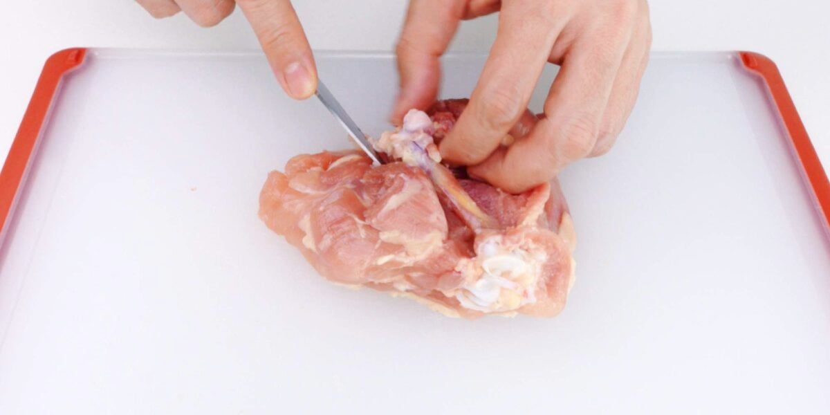 Cutting around the chicken thigh bone.