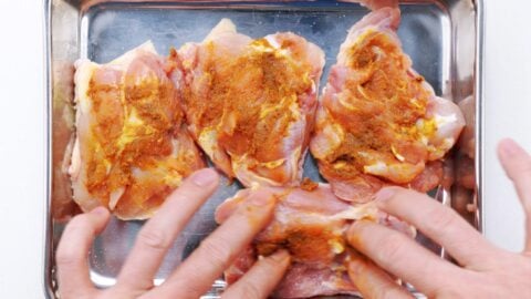 Spreading garlic curry paste onto chicken thighs.