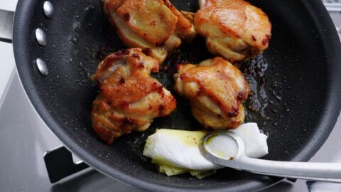 Draining excess oil from a frying pan with chicken.