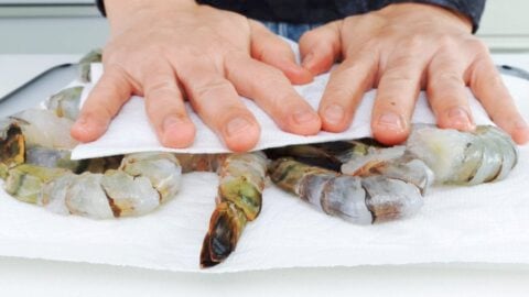 Patting shrimp dry with paper towels.