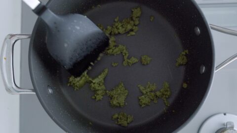 Frying green curry paste in a pot with a black spatula.