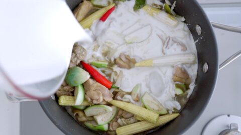 Adding baby corn, eggplant, chilies, bamboo, and coconut milk to green curry.