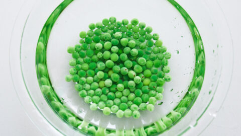 Chilling green peas in cold water in a glass bowl on a white surface to make green pea pesto.