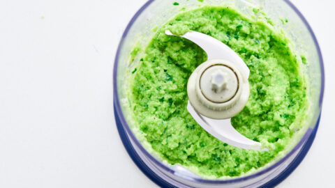 Green pea pesto with cheese and scallions in a blender on a white counter.