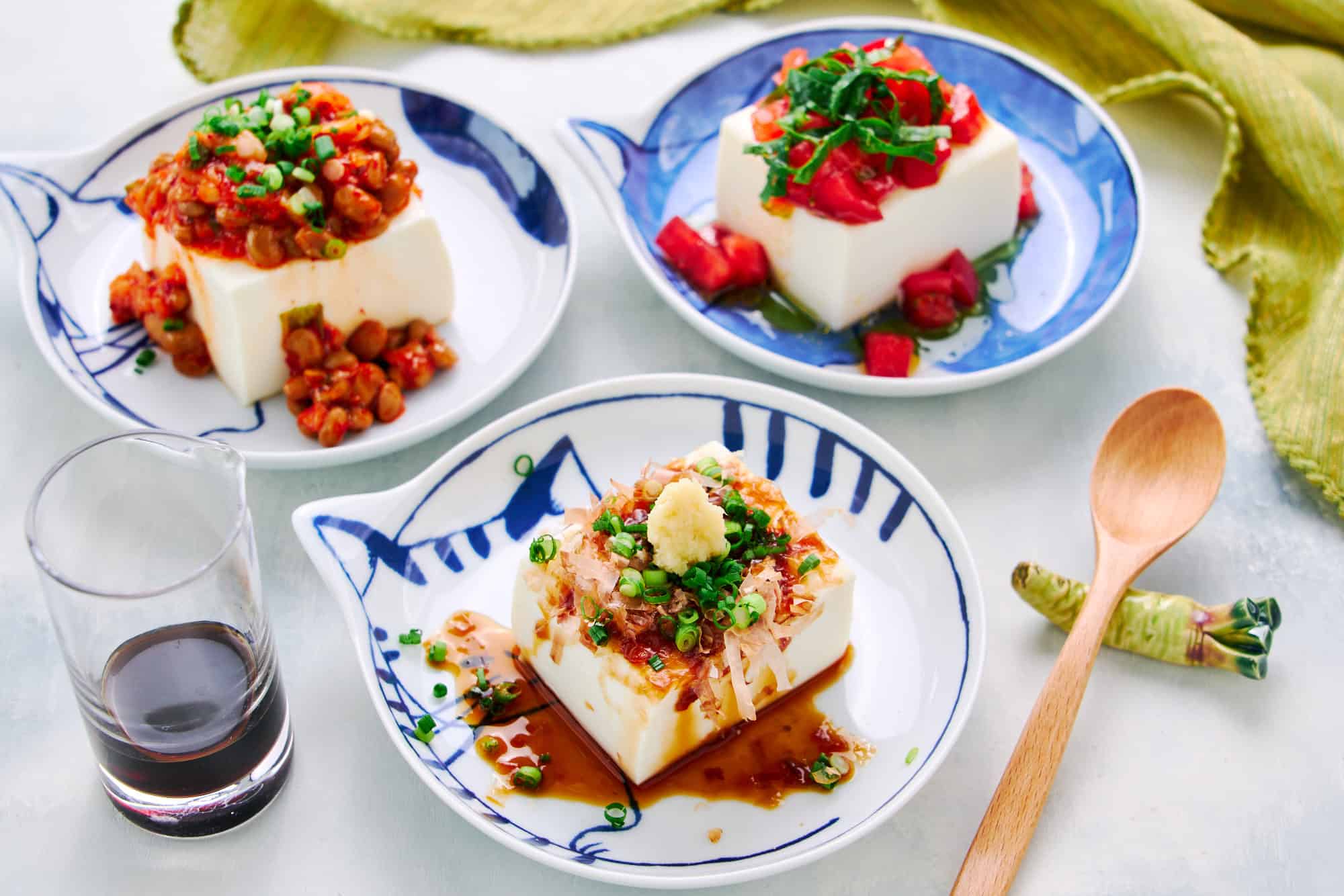 A wider shot of traditional Japanese Hiyayakko or cold tofu salad. In the background are two alternative versions - kimchi natto and Caprese Salad.