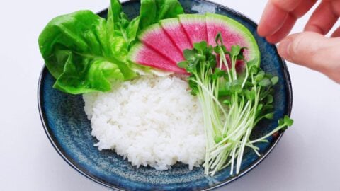 Layering vegetables on a bowl of cooked rice.