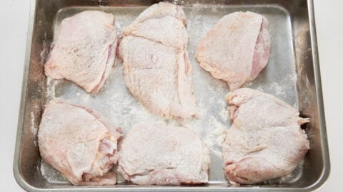 Chicken thighs dusted with flour on a tray for making honey lemon chicken.