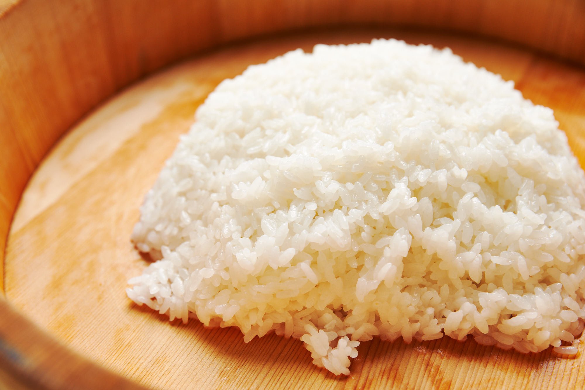 Mound of sushi rice in a traditional wooden sushi oke.