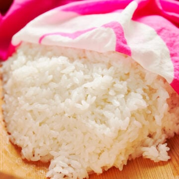 Sushi rice covered in a damp pink dishcloth to prevent it from getting dried out.